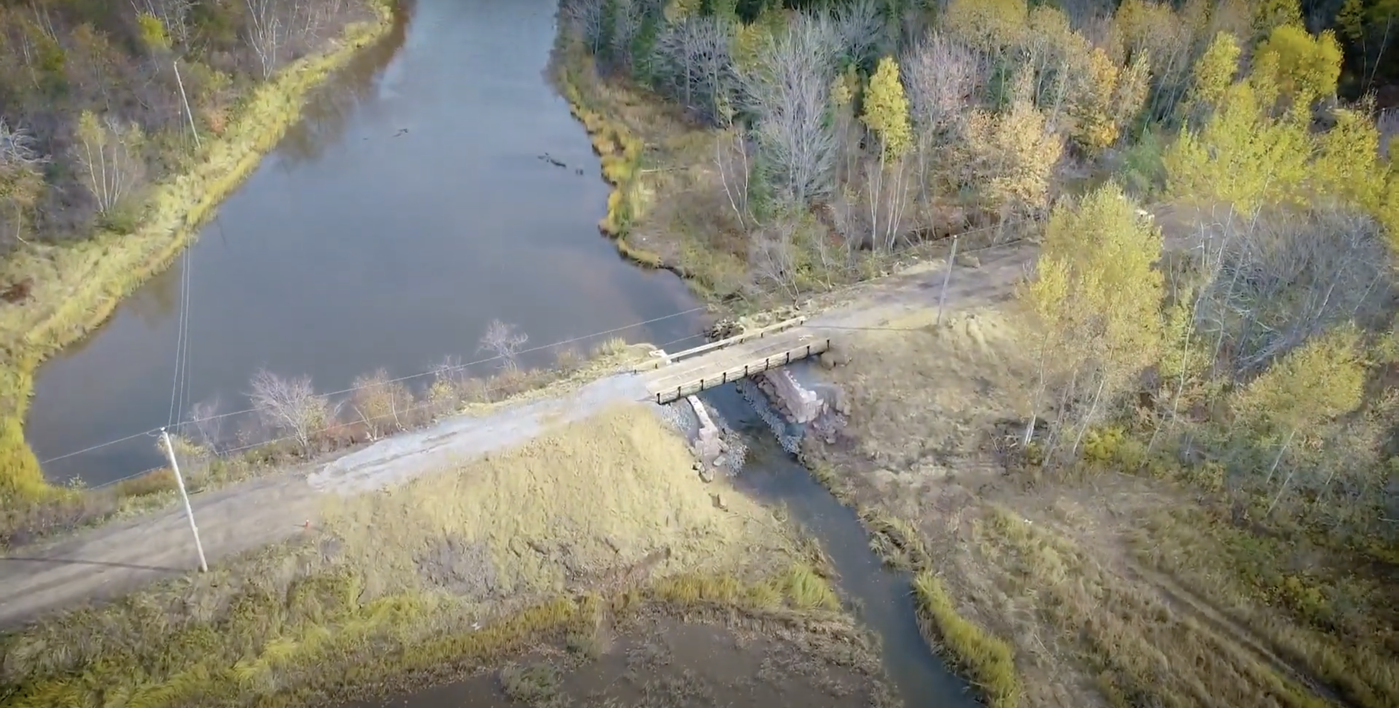 Vue aérienne d'une rivière. Un pont terrestre traverse la majeure partie de la rivière, mais il y a une petite ouverture sur le côté gauche où l'eau continue, avec un pont qui traverse cette brèche. 