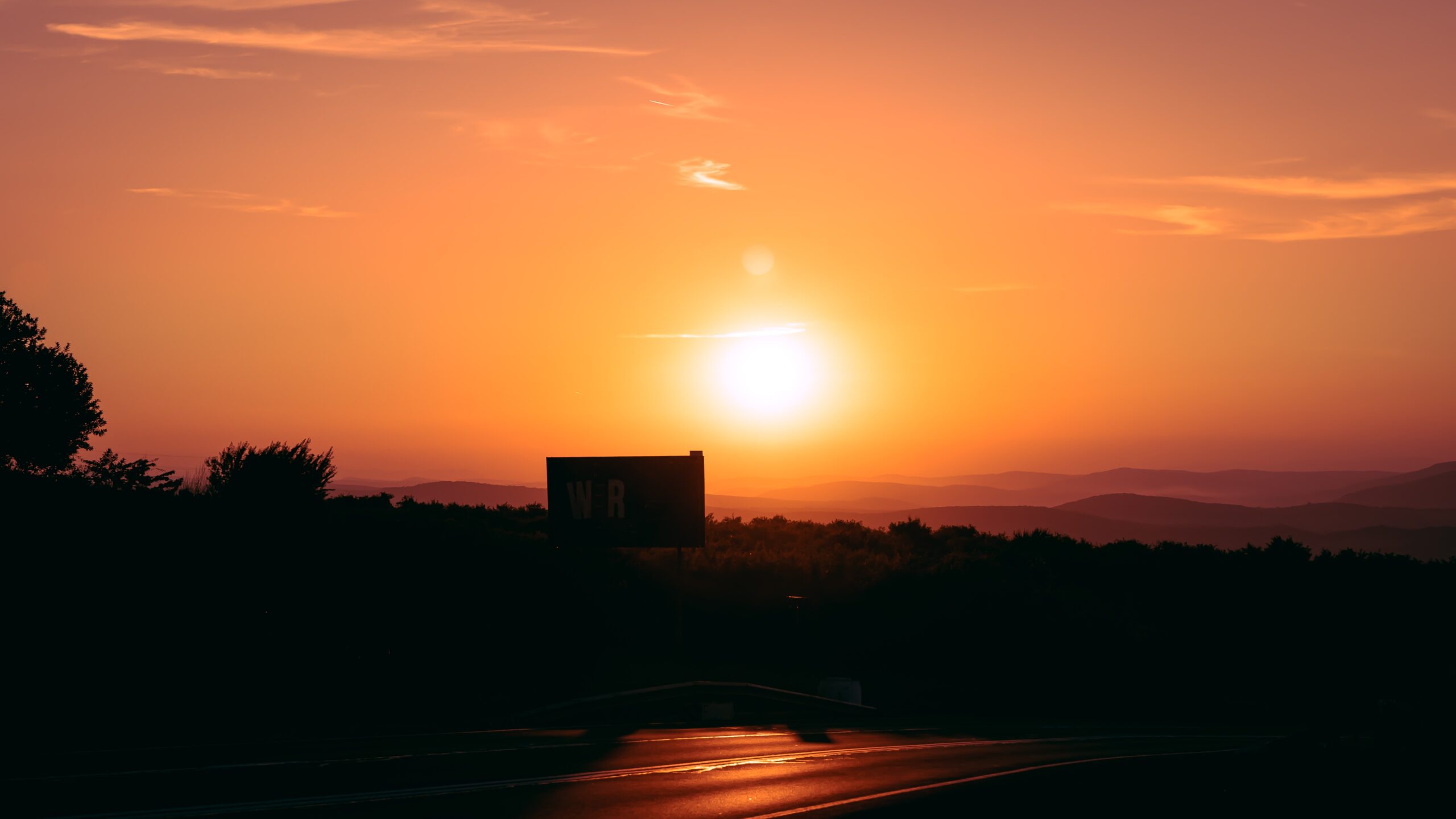 An orange sunset over a landscape with hills, trees, and a road. 