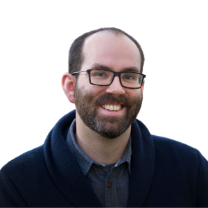 Le français suit. A picture of a person with short brown hair wearing glasses and a dark blue shirt smiling at the camera, framed by a blue circle.Photo d'une personne aux cheveux bruns courts, portant des lunettes et une chemise bleu foncé, souriant à l'appareil photo, encadrée d'un cercle bleu.