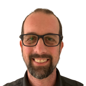 Le français suit. A picture of a person with short brown hair wearing glasses and a dark shirt smiling at the camera, framed by a green circle.Photo d'une personne aux cheveux bruns courts, portant des lunettes et une chemise sombre, souriant à l'appareil photo, encadrée d'un cercle vert.