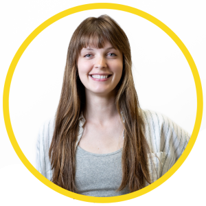 Le français suit A picture of a person with long dark brown hair wearing a grey top smiling at the camera, framed by a yellow circle. La photo d'une personne aux longs cheveux bruns, vêtue d'un haut gris, souriant à l'appareil photo, encadrée d'un cercle jaune.