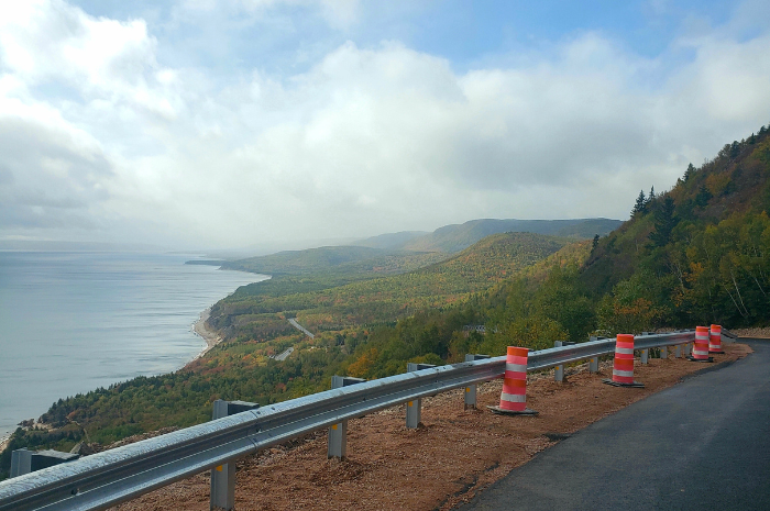 Le français suit. A roadside view of a forest and coastline, with a blue sky. Vue depuis la route sur une forêt et le littoral, sous un ciel bleu.